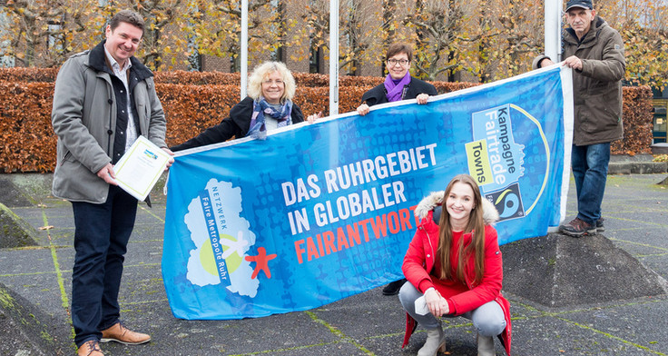 Vier Personen halten eine Flagge mit der Aufschrift "Das Ruhrgebeit in globaler Fairantwortung", davor hockt eine junge weibliche Person