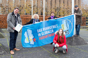 Vier Personen halten eine Flagge mit der Aufschrift "Das Ruhrgebeit in globaler Fairantwortung", davor hockt eine junge weibliche Person